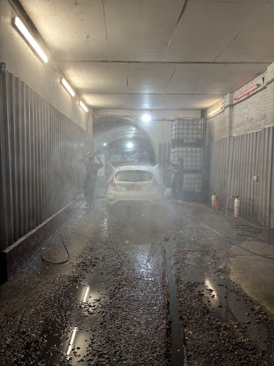 The Miami Car Wash bay under the railway arch, a car being pressure rinsed in the steam