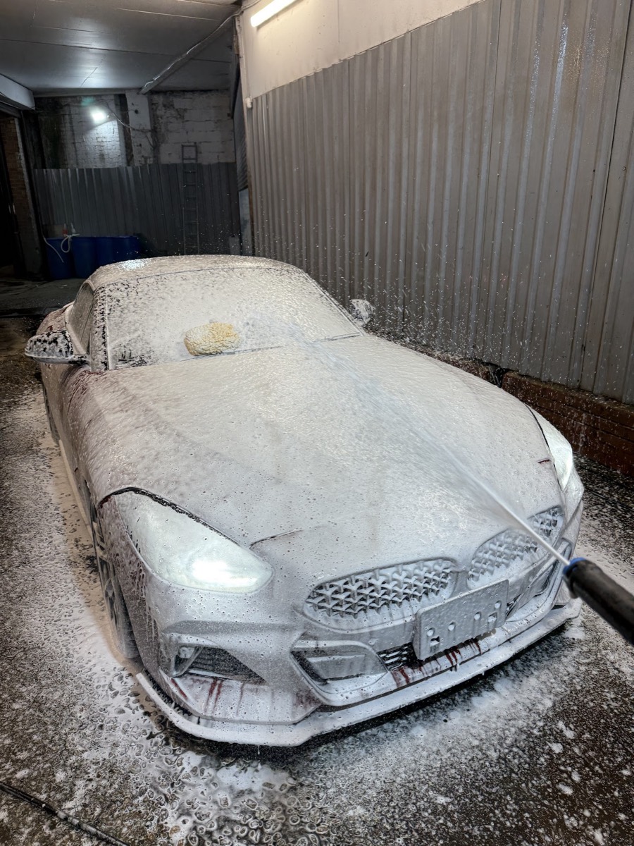 A car covered in thick snow foam being rinsed under the arches at Miami Car Wash, Bow